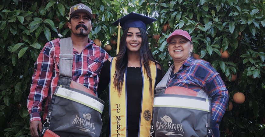 Anna Ocegueda stands between her parents in front of an orange grove