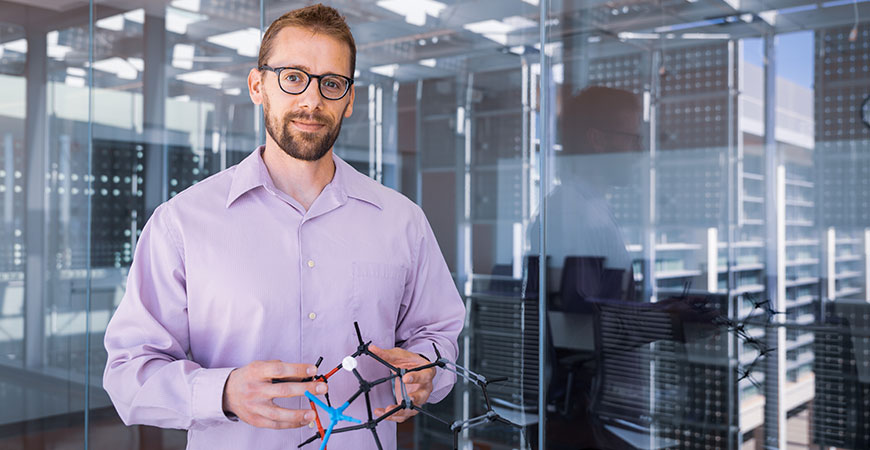 Professor Ryan Baxter posing in front of a glass separator