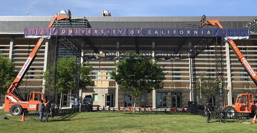 Workers construct the Commencement set using cherry pickers