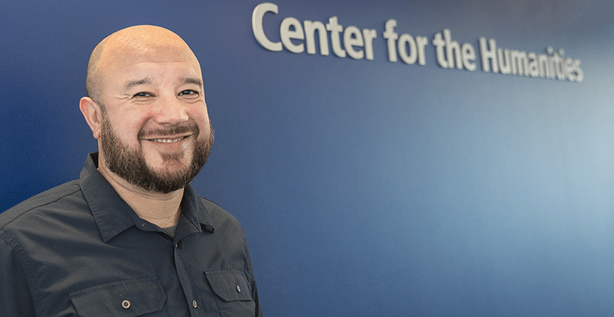 Professor Mario Sifuentez poses in front of Center for the Humanities signage