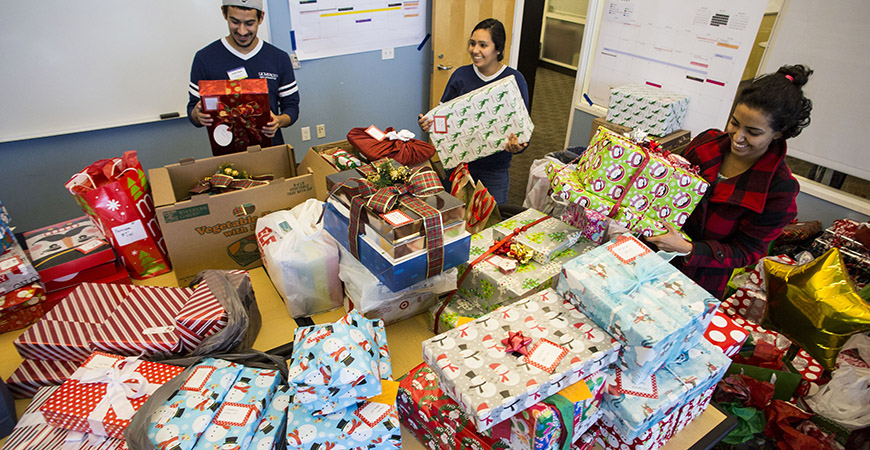 Three students organize table stacked with gift boxes