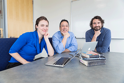 Three faculty members posing from a meeting table