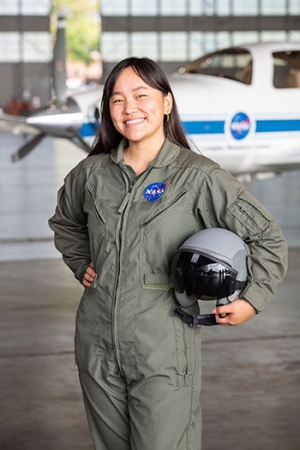 Lum wearing an official NASA flight suit tucking a helmet under her arm