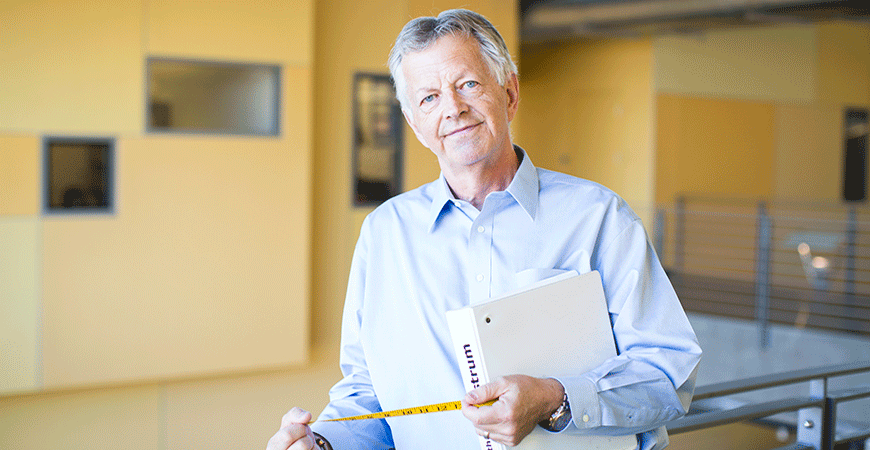 Professor Jan Wallander posing with a measuring tape and binder