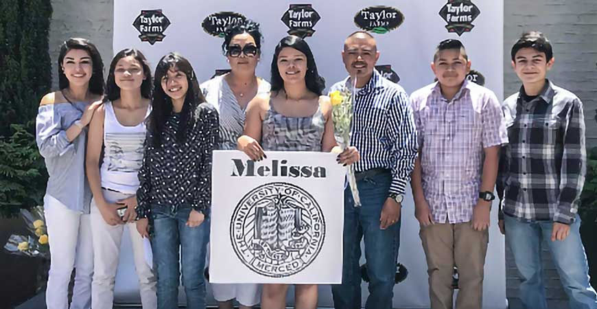 Second-year student Melissa Rios-Arias holds an image of UC Merced's seal while flanked by family members and friends.