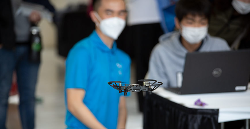 Peter Sou ('22) helps a student program a drone to fly a pattern at the Tri Valley Innovation Fair