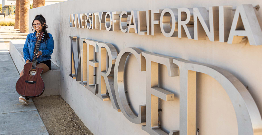 Student Cathryn Flores poses in front of a University of California, Merced sign.
