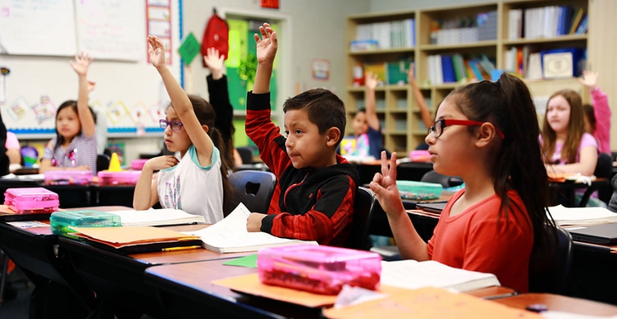 Young students raise their hands while seated in a classroom