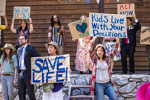 Actors holding up signs for eco-preservation around a man wearing a business suit